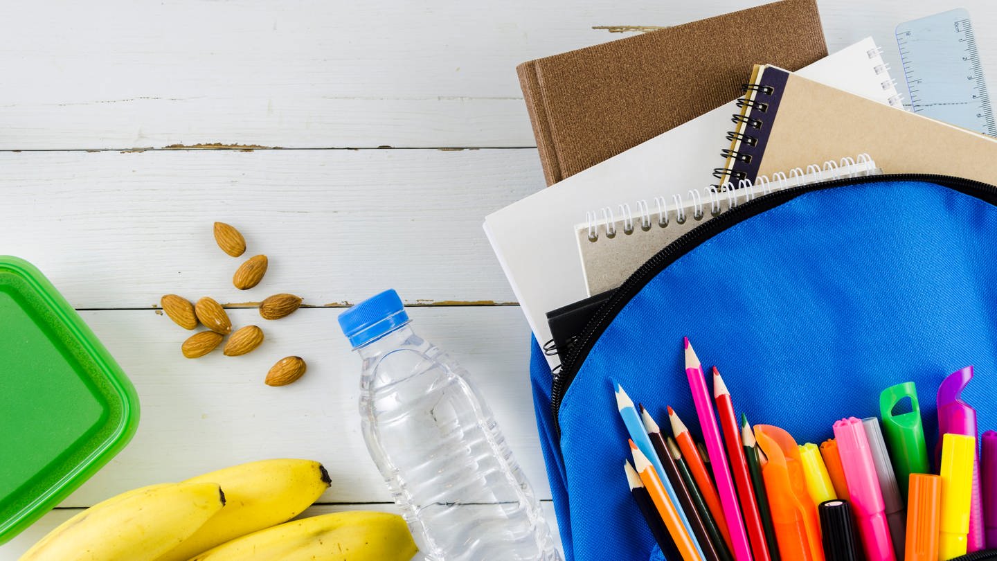 Symbolbild: Eine Schultasche mit Wasser, Banane, Nüssen und Stiften.