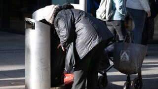 Eine Frau sucht in einem Mülleimer nach Leergut.