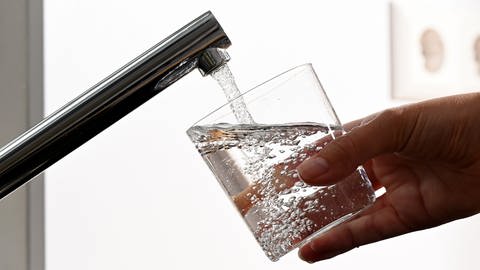 Kopfschmerzen: Eine Hand hält ein Wasserglas unter einen Wasserhahn. Der Grund: Viel Trinken ist gesund und hilft gegen Spannungskopfschmerzen.