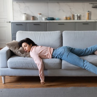 SYMBOLBILD: Eine Frau in rosa Bluse und Jeans liegt erschöpft auf der Couch.