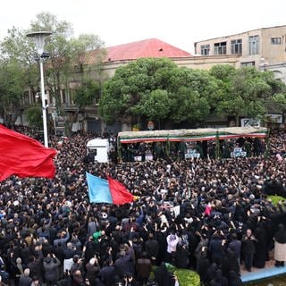 Menschen nehmen an der Trauerfeier für den verstorbenen Ebrahim Raisi teil. Ein Lkw bewegt sich langsam durch die Menge.