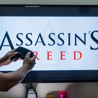 Man holding steam controller in front of a screen loading a game of assassin s creed an action adventure game by ubisoft with multiple installements 