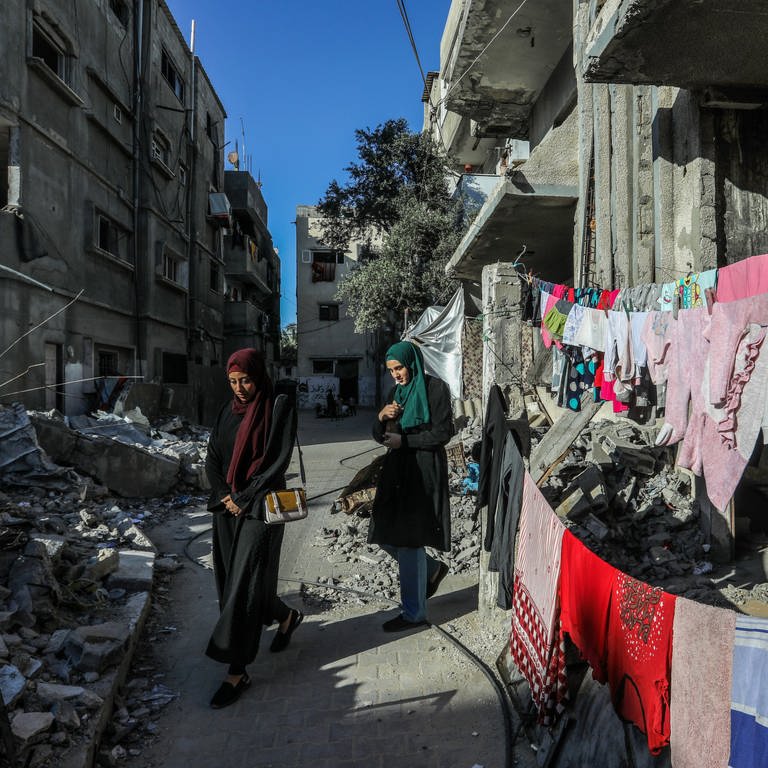 Vertriebene Palästinenserinnen aus der Stadt Rafah, die vor den Kämpfen fliehen, gehen während der anhaltenden Kämpfe zwischen Israel und der Hamas an einem von israelischen Kampfflugzeugen zerstörten Gebäude vorbei.