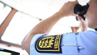 Symbolbild: Ein Polizist von der Wasserschutzpolizei schaut auf dem Bodensee auf dem Boot durch ein Fernglas.