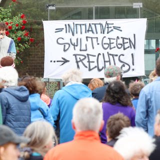 Teilnehmer stehen bei einer Kundgebung vor dem Rathaus in Westerland, wo ein Transparent mit dem Schriftzug „Initiative Sylt gegen Rechts angebracht wurde“. 