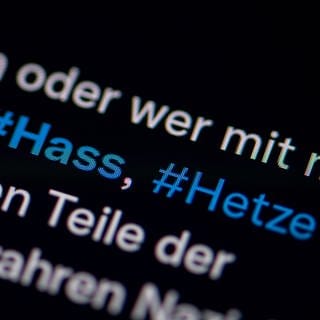 Auf dem Bildschirm eines Smartphones sieht man die Hashtags Hass und Hetze in einem Twitter-Post. 