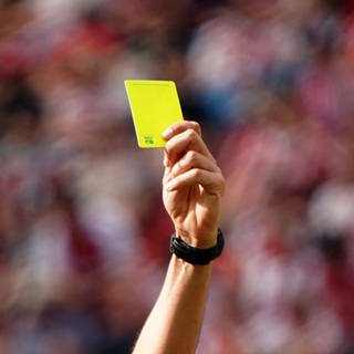 Der Arm eines Fußball-Schiedsrichters hält eine Gelbe Karte in die Luft (Symbolbild)