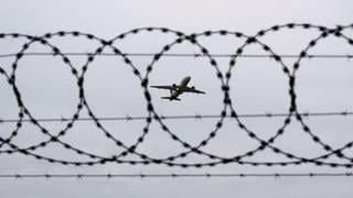 Ein Flugzeug startet am Flughafen Hannover - fotografiert durch Stacheldraht am Flughafenzaun.