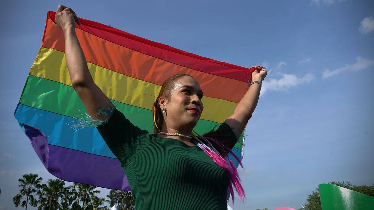 Eine Frau hält die Pride-Flagge in die Luft.