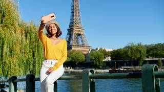 Eine junge Frau macht ein Selfie vor dem Eiffelturm in Paris.