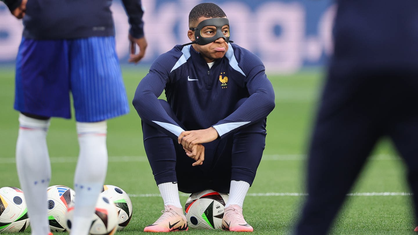 Frankreichs Kylian Mbappe sitzt mit einer Schutzmaske nach seinem Nasenbeinbruch auf einem Ball beim Aufwärmen