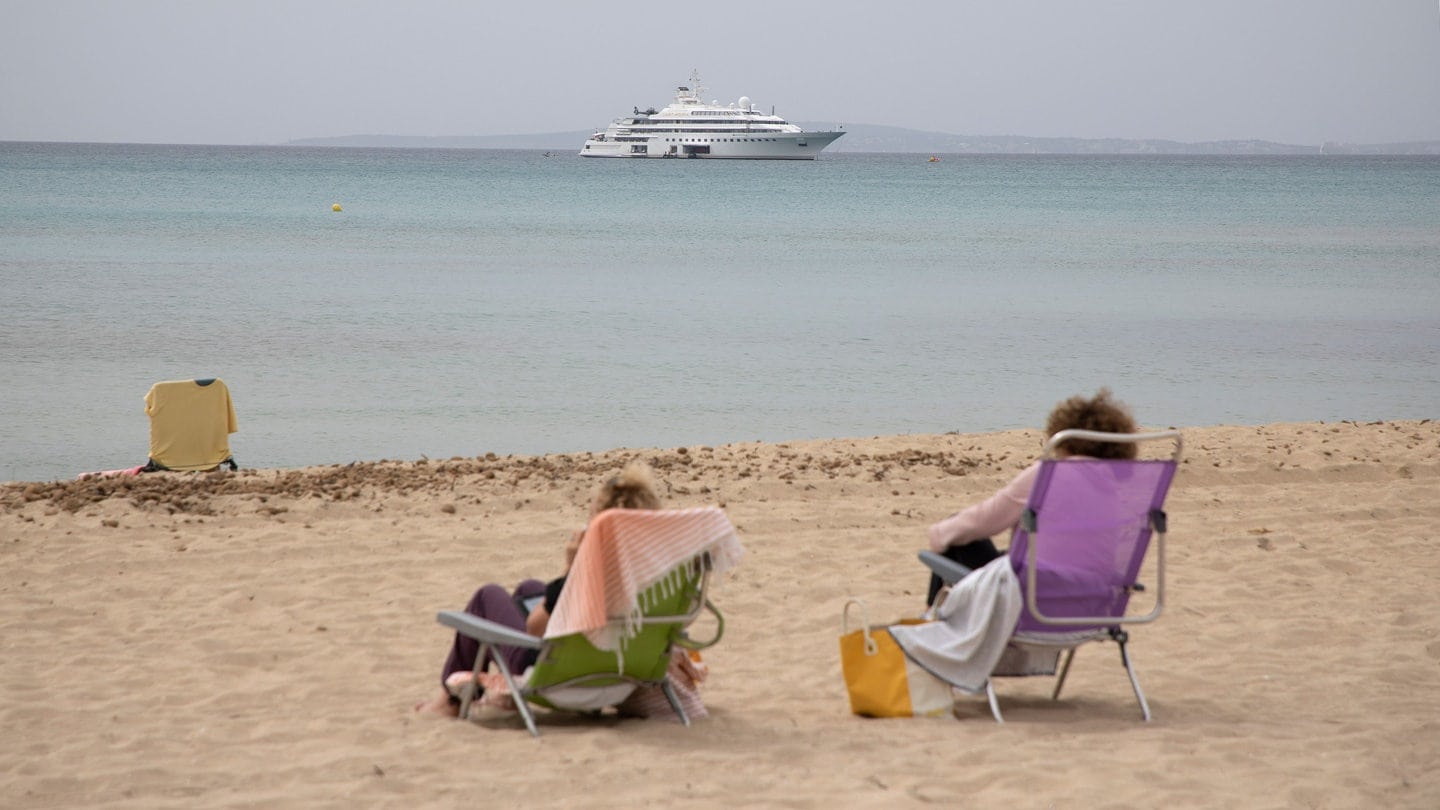 SYMBOLBILD - Frauen sitzen an einem Strand. Auf dem Meer ist eine Jacht zu sehen.