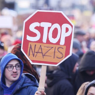 Teilnehmer der Demonstration ziehen durch die Stadt und halten ein Plakat mit der Aufschrift "Stop Nazis" hoch (Symbolbild)