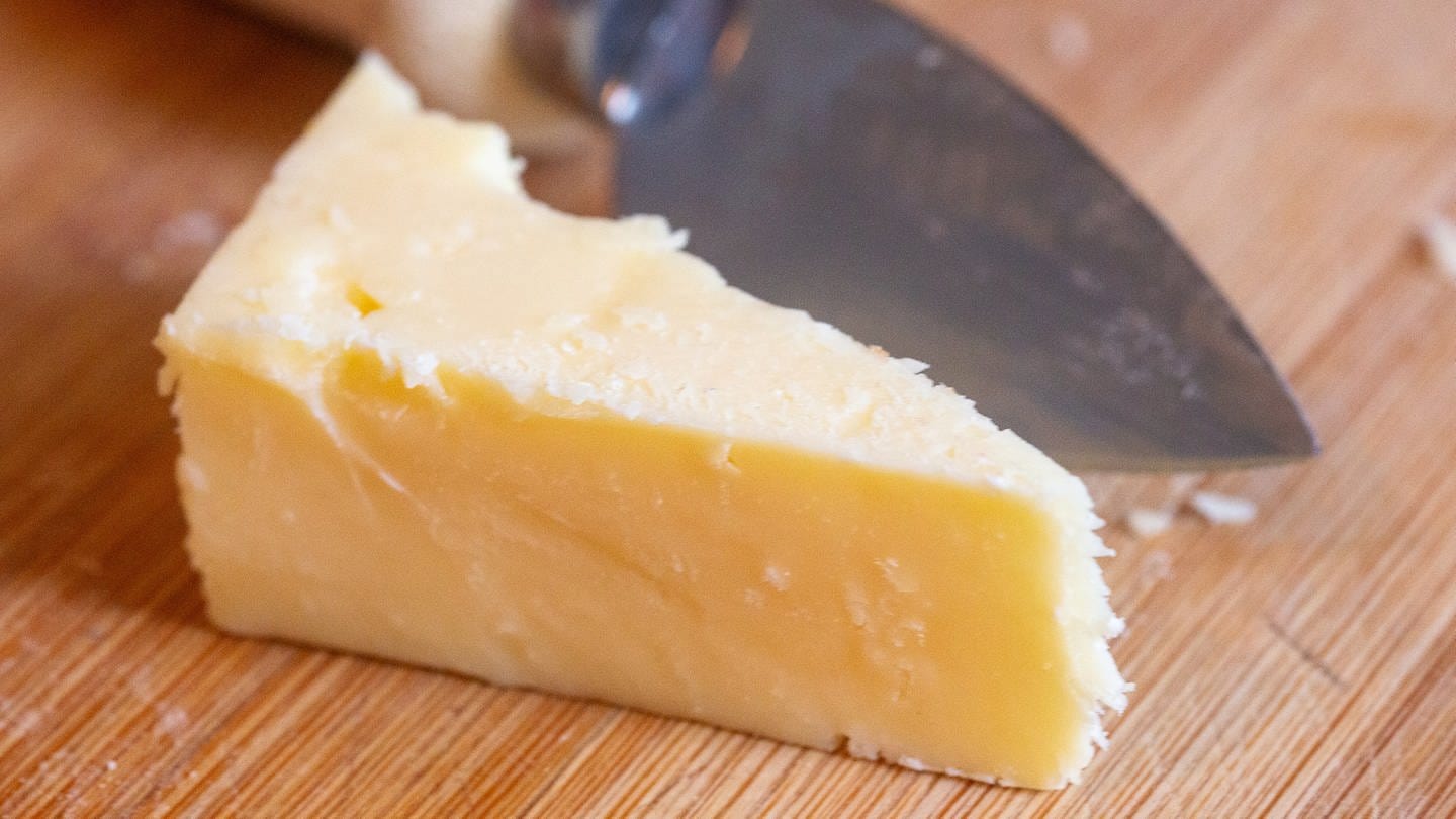 Ein Stück Cheddar-Käse liegt auf einem Brett.