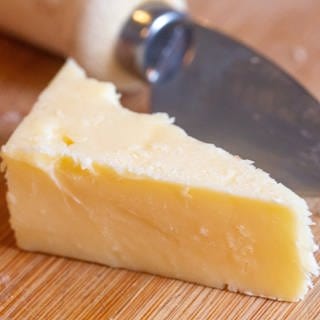 Ein Stück Cheddar-Käse liegt auf einem Brett. 
