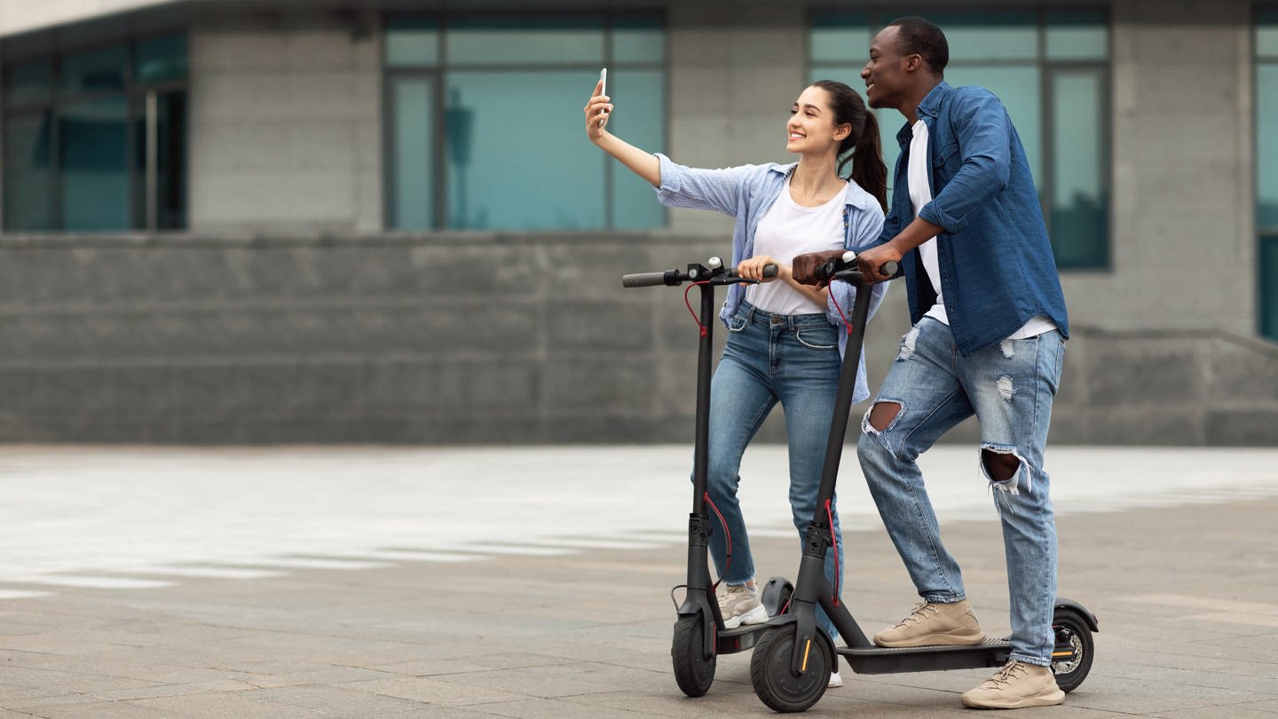 Ein Paar macht ein Selfie zwei E-Scootern (Symbolbild).
