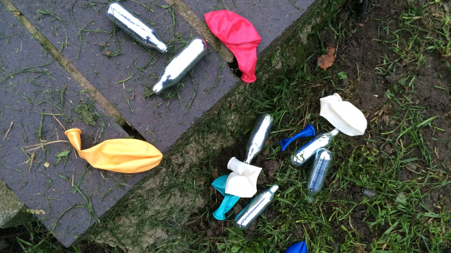 Lachgas-Kartuschen und Luftballons liegen in einem Park. Gesundheitsminister Lauterbach will den Lachgasverkauf an Jugendliche jetzt verbieten.