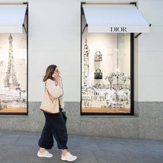 Eine Frau läuft an Schaufenstern von einem Dior-Laden vorbei - Gegen Dior und Armani wird jetzt wegen möglicher Ausbeitung von Mitarbeitern ermittelt.