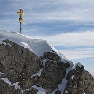 Die im Tal restaurierten Strahlen des Gipfelkreuzes der Zugspitze wurden von Mitarbeitern wieder am Gipfelkreuz angebracht. Am Sonntag ist ein 18-jähriger Mann bei einem Unwetter tödlich verletzt worden. Ein Blitz ist mehrmals heftig eingeschlagen.