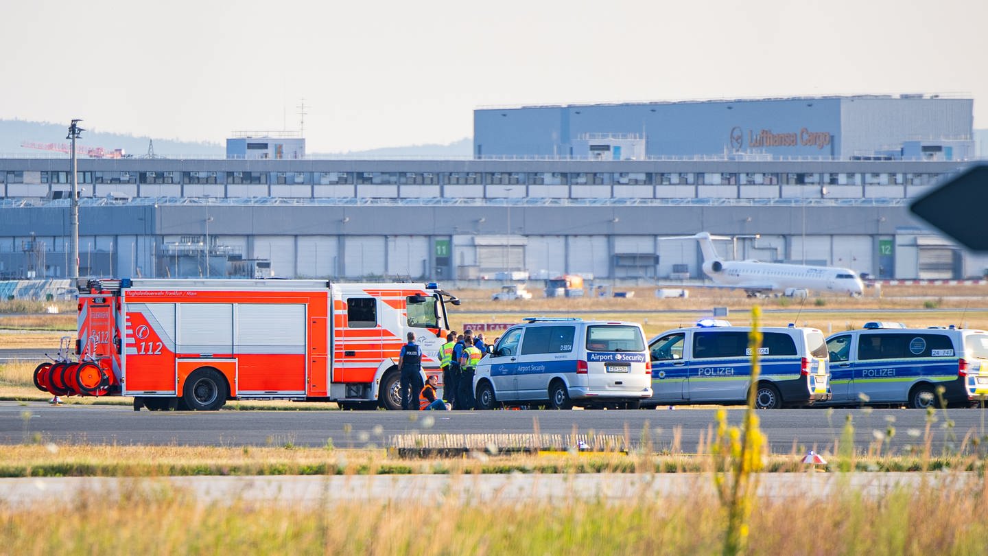 Einsatzfahrzeuge der Polizei stehen am Frankfurter Flughafen bei einer Aktion von Klimaaktivisten. Mehrere Demonstranten waren am frühen Morgen auf das Gelände des Flughafens eingedrungen und hatten sich festgeklebt. Der Flugverkehr ist vorläufig eingestellt worden, teilte ein Sprecher der Bundespolizei mit.