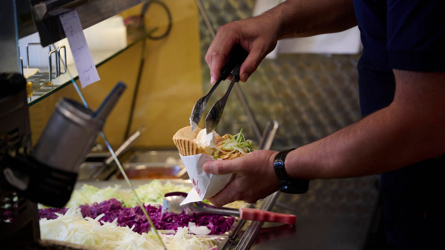 Ein Mitarbeiter eines Döner Schnellimbisses füllt eine Dönertasche.