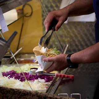 Ein Mitarbeiter eines Döner Schnellimbisses füllt eine Dönertasche.