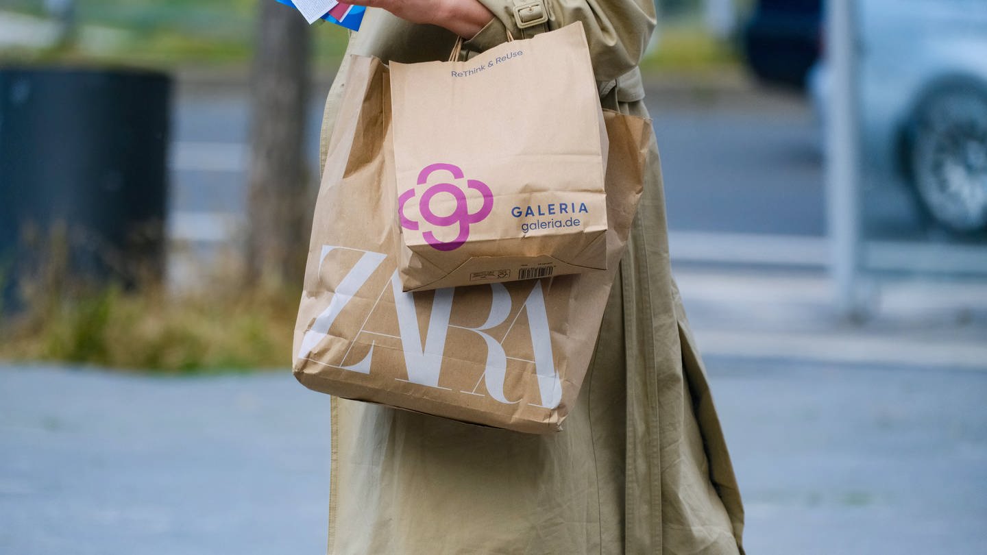 Eine Frau trägt zwei Einkaufstüten durch die Stadt: Eine Tüte vom Zara, die andere von Galeria.