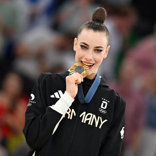 Darja Varfolomeev, in schwarzem Trikot, mit Aufschrift "Germany" beißt auf ihre Goldmedaille. 