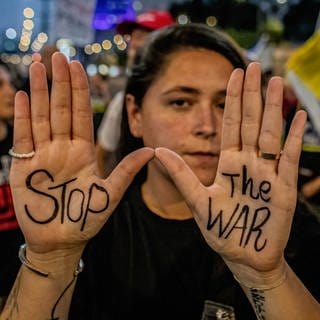 Eine junge Frau zeigt während einer Kundgebung die Innenflächen ihre Hände, auf denen "Stop the War" geschrieben steht. Bei den aktuellen Verhandlungen geht es erneut um eine Waffenrufe und die Freilassung der Geiseln.