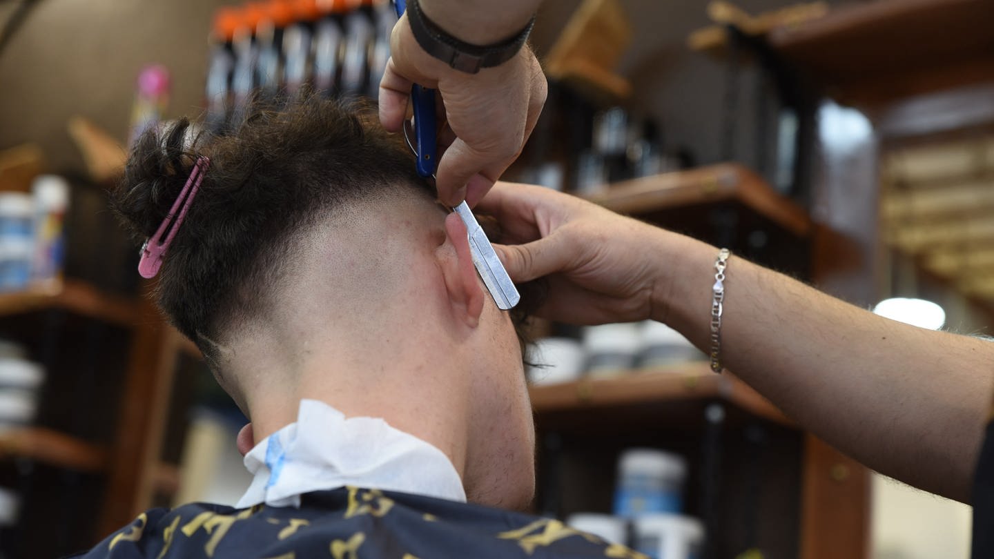 Ein Friseur rasiert in einem Barbershop die Haare eines männlichen Kunden.