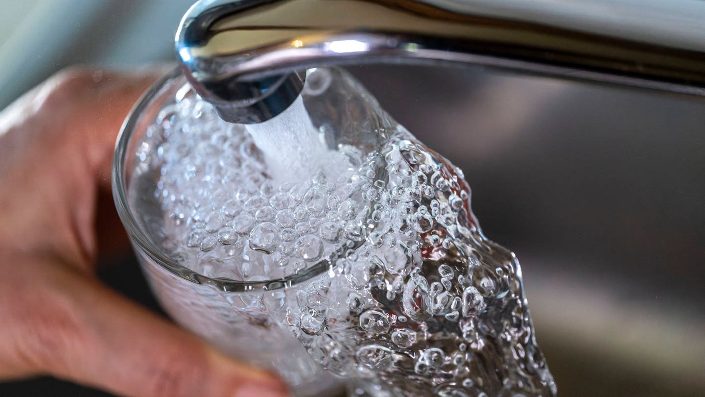 Trinkwasser läuft aus dem Wasserhahn einer Küche in ein Glas.