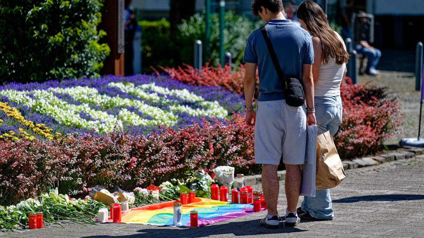 Nach der Messerattacke auf dem Solinger Stadtfest legen Menschen in der Nähe des Tatortes Blumen neben einer Regenbogenflagge nieder.