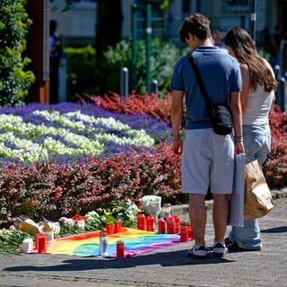 Nach der Messerattacke auf dem Solinger Stadtfest legen Menschen in der Nähe des Tatortes Blumen neben einer Regenbogenflagge nieder.