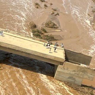 Der Arbaat-Staudamm im Sudan ist nach heftigen Regenfällen gebrochen. Menschen stehen auf dem kaputten Damm.