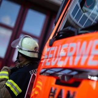 Eine Einsatzkraft der Feuerwehr steht neben einem Feuerwehrauto.