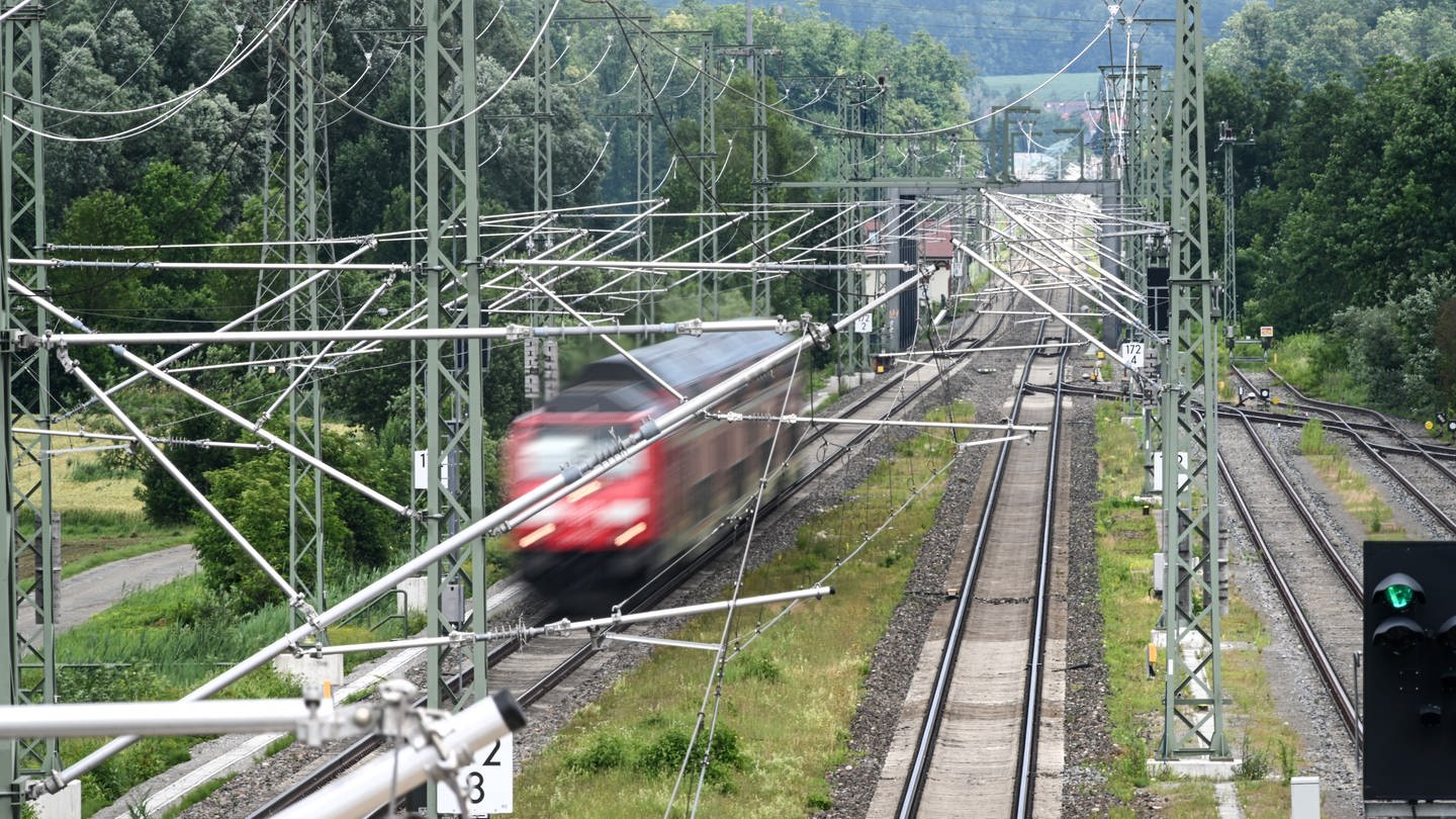 Ein Zug fährt auf den Schienen - darüber sind Oberleitungen zu sehen.