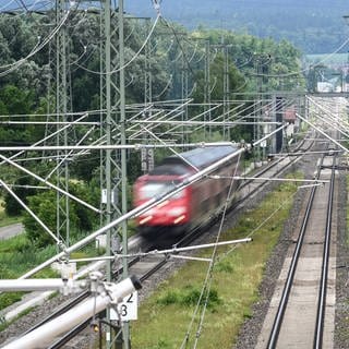 Ein Zug fährt auf den Schienen - darüber sind Oberleitungen zu sehen.