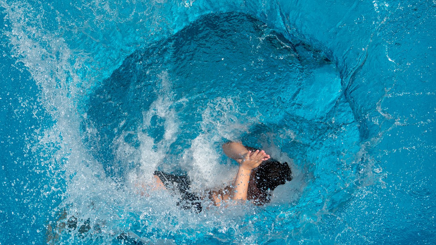 Ein Jugendlicher springt vom Sprungturm ins Wasser.