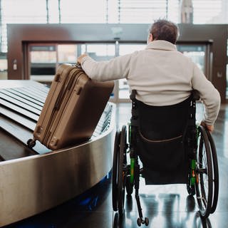 Ein Mann im Rollstuhl holt sein Gepäck ab am Flughafen.