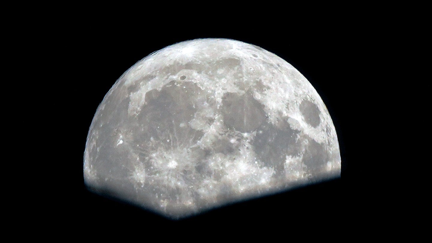 Ein fast voller Supermond erhebt sich hinter einem Wohnhaus nach Regen.