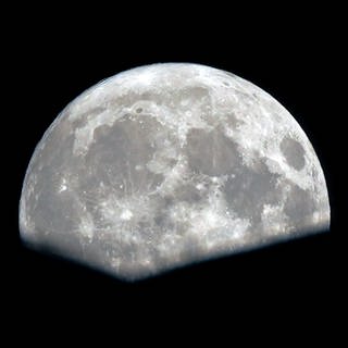 Ein fast voller Supermond erhebt sich hinter einem Wohnhaus nach Regen.