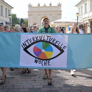 Eine Gruppe hält vor dem Brandenburger Tor ein Banner mit "Interkulturelle Woche" hoch.