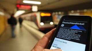 Fahrgast hält ein Smartphone mit einem digitalen Deutschlandticket an einer U-Bahnstation in der Hand: Das Deutschlandticket wird ab 2025 teurer.