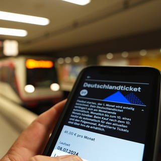 Fahrgast hält ein Smartphone mit einem digitalen Deutschlandticket an einer U-Bahnstation in der Hand: Das Deutschlandticket wird ab 2025 teurer.