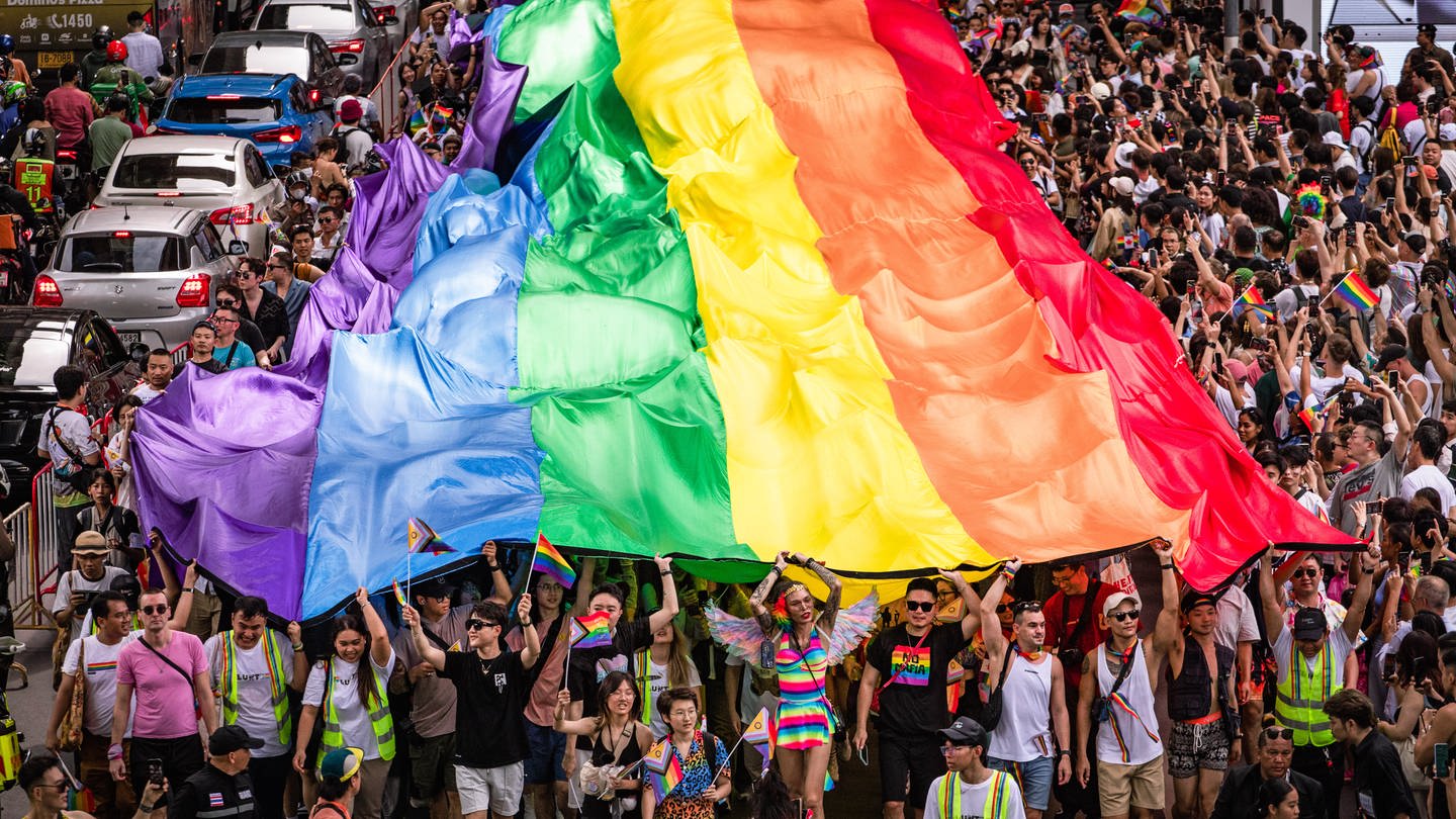 Menschen in Thailand gehen mit einer riesigen Pride-Flagge auf die Straße.