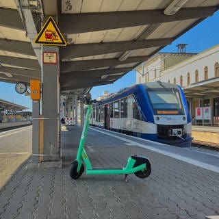 Ein E-Roller vor einer einfahrenden Bahn.