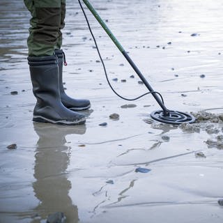 Mann mit Metalldektektor sucht Schatz am Strand.