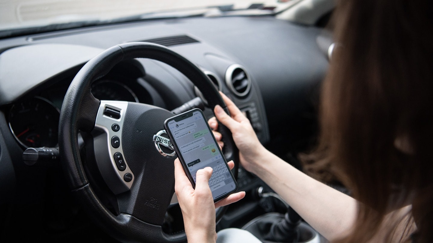 Eine Frau sitzt mit Handy am Steuer (gestellte Szene).