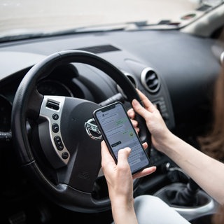 Eine Frau sitzt mit Handy am Steuer (gestellte Szene).