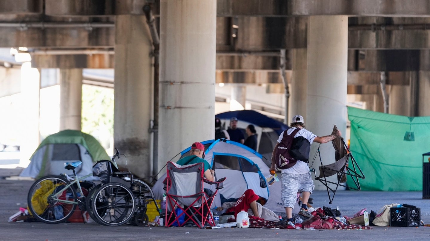 Menschen, die in einem Obdachlosenlager leben, heben ihre Habseligkeiten auf, nachdem die Polizei des Bundesstaates Louisiana sie angewiesen hat, sich an einen anderen, vorher festgelegten Ort zu begeben, während sie eine Razzia im Vorfeld eines Taylor Swift-Konzerts durchführt.